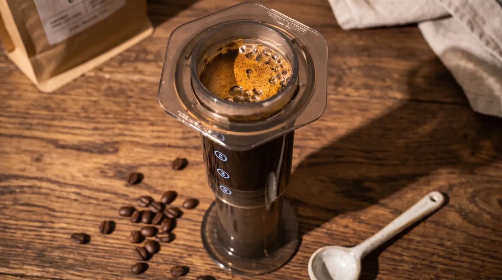 Inverted AeroPress mid-flip, motion frozen against a soft, bright backdrop.