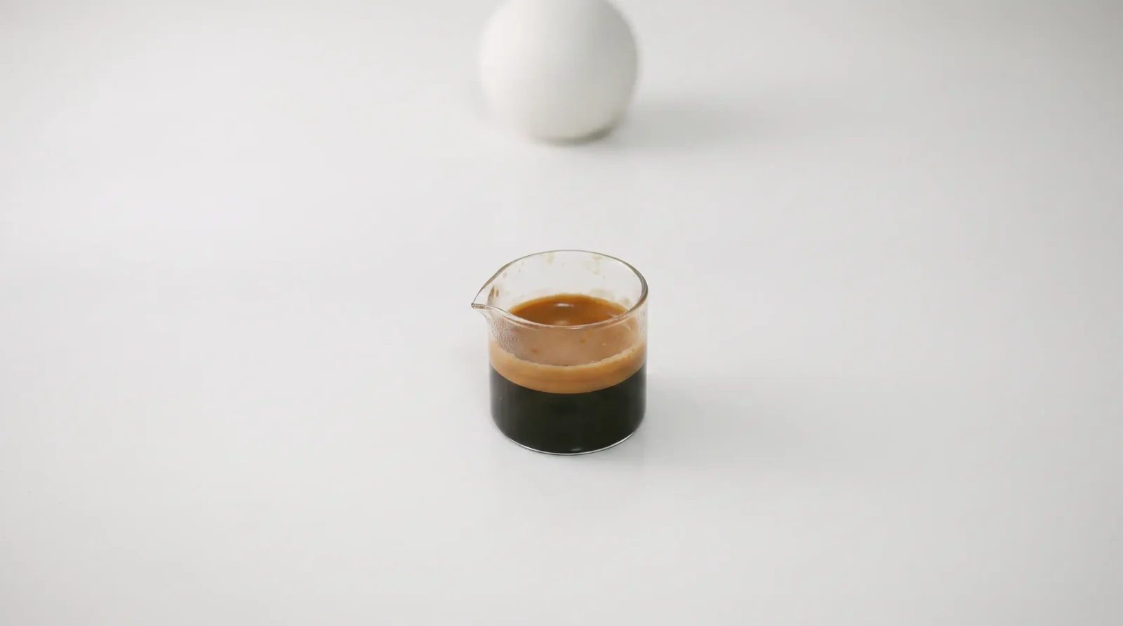 Bottomless portafilter in macro, tiger-striped espresso flowing against a soft pale backdrop.